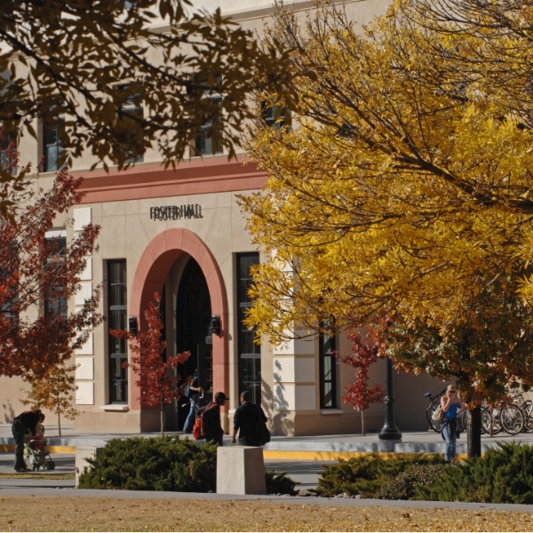 Autumn view of Foster Hall with a red-trimmed arched entrance, colorful trees, pedestrians, and bicycles.